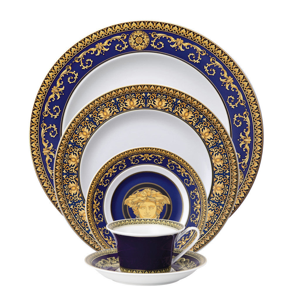 A 5-piece Versace Medusa Blue dinnerware set, including a dinner plate, salad plate, bread and butter plate, tea cup, and tea saucer, with blue and gold ornamental patterns.
