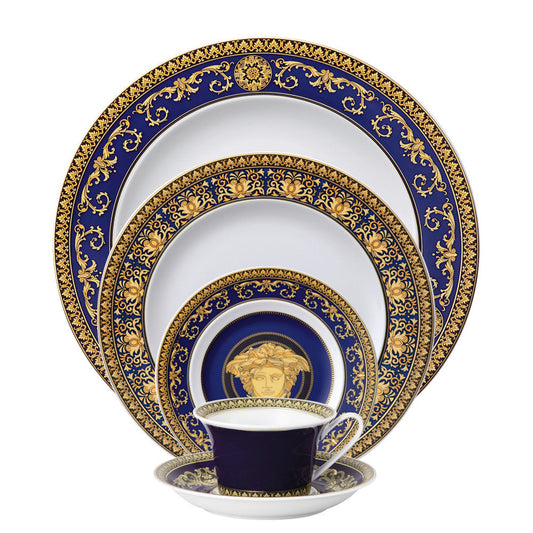 A 5-piece Versace Medusa Blue dinnerware set, including a dinner plate, salad plate, bread and butter plate, tea cup, and tea saucer, with blue and gold ornamental patterns.