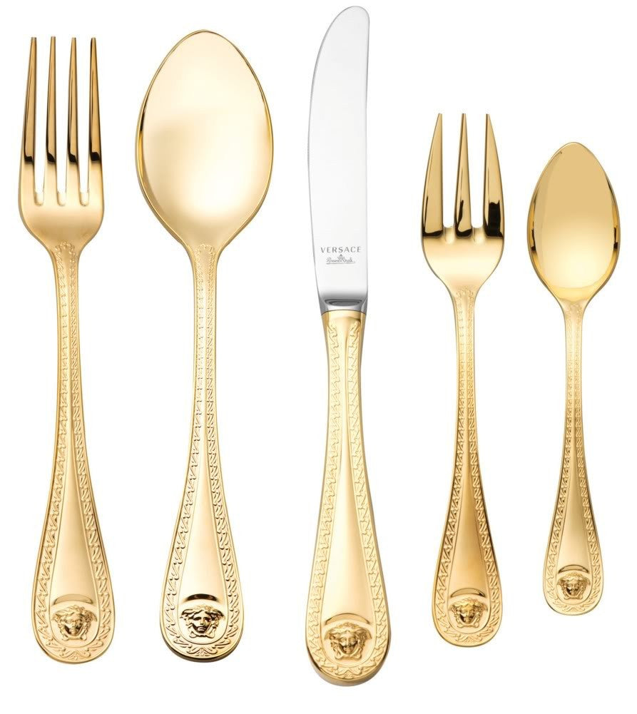 A collection of Versace Medusa Gold flatware, including dinner spoons, dinner forks, dinner knives, coffee spoons, and cake forks, displayed against a white background.