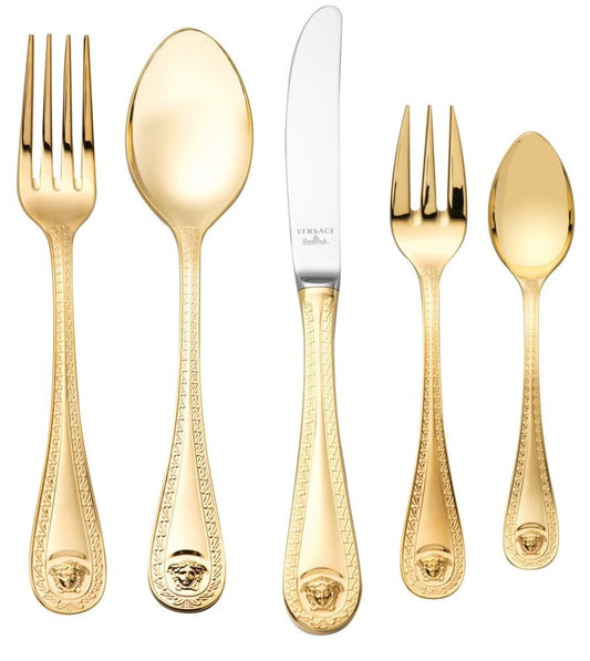 A collection of Versace Medusa Gold flatware, including dinner spoons, dinner forks, dinner knives, coffee spoons, and cake forks, displayed against a white background.